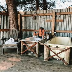 a woman sitting in an outdoor bathtub next to a tree and two chairs on the deck