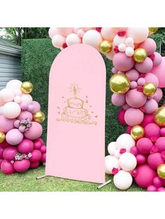 a pink and gold balloon arch in the grass