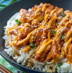 a black plate topped with rice and meat covered in gravy next to chopsticks