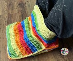 a person holding onto a multicolored crocheted blanket on the floor next to a button