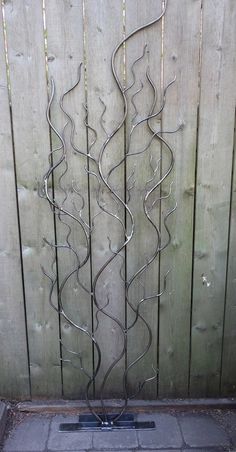 a tall metal sculpture sitting in front of a wooden fence