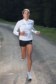 a woman running down a dirt road next to trees