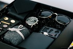 an open black box containing sunglasses, tie and other items to be used as a watch