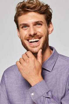 a man with a goatee smiles and holds his hand to his chin while wearing a purple shirt