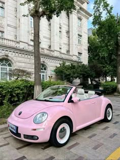 a pink convertible car parked in front of a large building