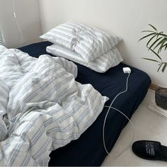 an unmade bed with two pillows and a plant in the corner next to it