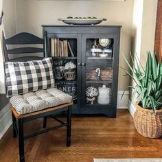 a black cabinet sitting next to a chair and a potted plant on top of a hard wood floor