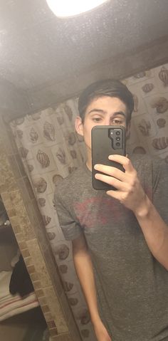 a young man taking a selfie in front of a mirror with his cell phone