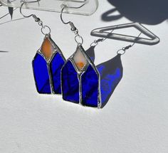 three blue and orange earrings sitting on top of a white table next to a pair of glasses