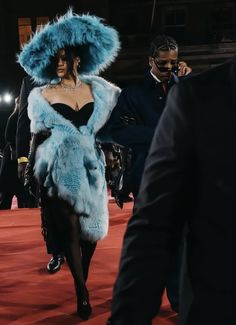 a woman in a blue fur coat and black dress walking down a red carpeted area