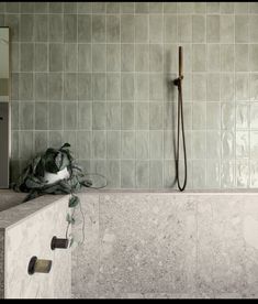 a white tiled bathroom with a shower head next to the bathtub and towel rack