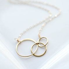 "This gold circle necklace is a great addition to any minimalist's style outfit. These three interlocking 14k gold-fill rings are a constant reminder that we are all connected in one form or another. Attached to a delicate gold fill chain with a spring-ring clasp, it's pure simplicity and perfect for any occasion! PRODUCT DETAILS * Chain and findings are 14k gold-fill * Circles measure 37mm (1 7/16\") by 18mm (11/16\") (in diameter they are 18mm (11/16\"), 15mm (9/16\") and 12mm (1/2\")) * Comes Sisters Necklace, Interlocking Rings, Minimalist Necklace Gold, Interlocking Ring, Gold Circle Necklace, Circle Jewelry, Mom Ideas, Cheap Engagement Rings, Minimalist Pendant