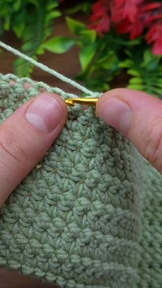 someone is holding the end of a crocheted piece of cloth with a needle in it