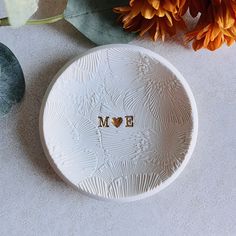 a white plate with the word mom written on it next to some flowers and leaves