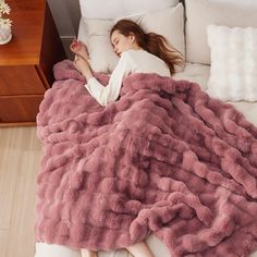 a woman laying on top of a bed covered in a pink fluffy blanket and pillows