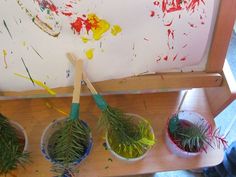 three buckets filled with green plants sitting on top of a wooden shelf next to paintbrushes