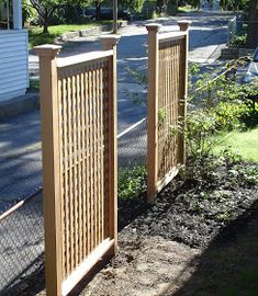 two wooden gates are next to each other on the side of a road in front of a house