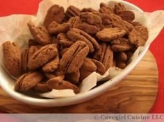 a white bowl filled with pecans sitting on top of a wooden table next to a red cloth