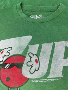 Keep up on your retro tee collection with our new 7UP tee featuring a faded 7UP graphic on a super soft Heather Kelly Green poly/cotton blend tee! Poly/Cotton Soft Touch Tee Machine Wash Tumble Dry Regular Fit Printed in USA Green Retro Graphic Design Top, Retro Green Tops With Front Print, Green Graphic Tee With Front Print, 7up Logo, Retro Green T-shirt With Logo Print, Green Graphic Cotton T-shirt, Green Relaxed Fit T-shirt With Back Print, Green Graphic Tee Cotton T-shirt, Soda Logo