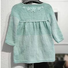 a green sweater hanging on a clothes hanger in front of a white painted wall