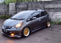 a small gray car with yellow rims parked in a parking lot next to a concrete wall