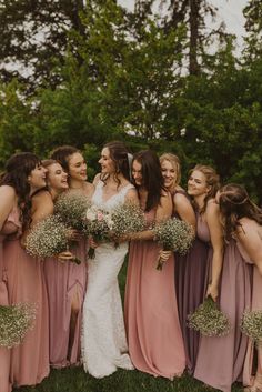 a group of women standing next to each other in front of trees and grass holding bouquets