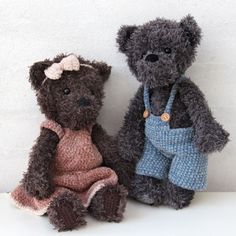 two teddy bears sitting next to each other on a white surface, one is wearing overalls and the other has a bow tie