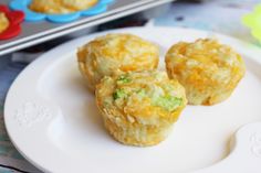 three small muffins on a white plate next to some colorful cups and spoons