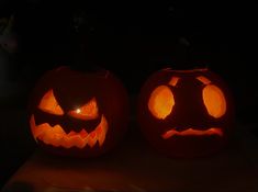 two carved pumpkins sitting on top of a table with their faces glowing in the dark