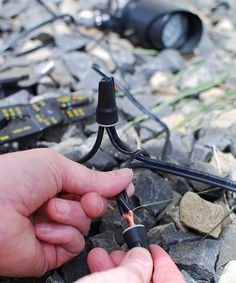 a hand holding a black wire connected to an electrical device on top of some rocks