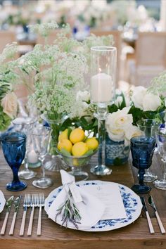 the table is set with blue and white dishes, silverware, lemons, and greenery