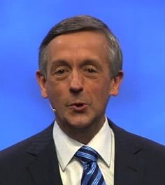 a close up of a person wearing a suit and tie in front of a blue background