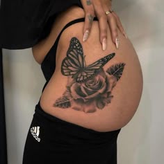 a woman's stomach with a butterfly and rose tattoo on the side of her belly