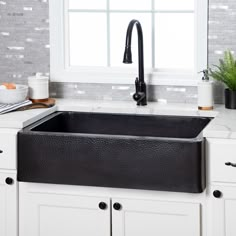 a black sink in a white kitchen next to a window with potted plants on the counter