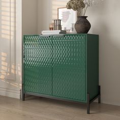 a green cabinet sitting next to a vase with flowers in it on top of a hard wood floor