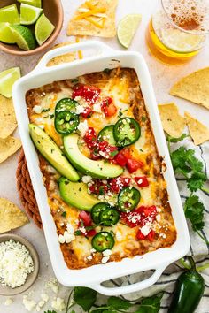 a white casserole dish filled with vegetables and cheese surrounded by tortilla chips