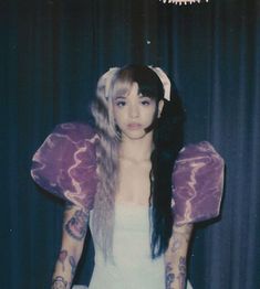 a woman with long hair wearing a purple butterfly wings costume and holding her hands behind her back