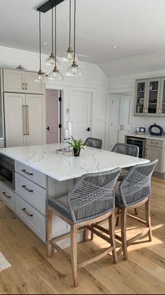 a kitchen with an island and chairs in the middle, surrounded by white cabinetry