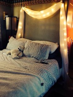 a teddy bear laying on top of a bed covered in white sheets and pillows with lights