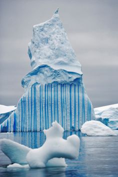 an iceberg floating in the water with snow on it's side and another large piece of ice behind it