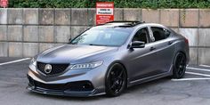 a silver acurace parked in a parking lot next to a wall and bushes