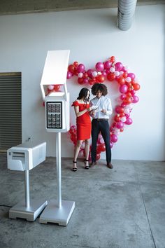 two people standing next to each other in front of a wall with balloons and a machine