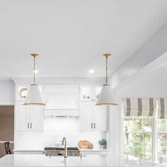 a large kitchen with white cabinets and marble counter tops, two pendant lights over the island