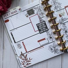 an open planner book sitting on top of a wooden table next to flowers and a pen