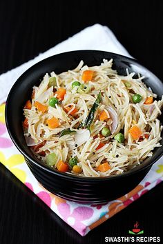 a black bowl filled with noodles and veggies on top of a colorful napkin