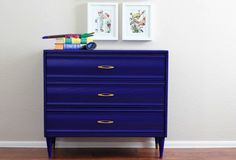 a blue dresser with two pictures on the wall above it and a pair of crayons