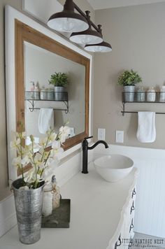 a white sink sitting under a bathroom mirror next to a metal bucket filled with flowers