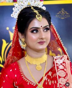 a woman wearing a red and gold bridal outfit with jewelry on her head, standing in front of a backdrop