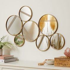 four circular mirrors mounted on the wall above a dresser with a vase and plant next to it