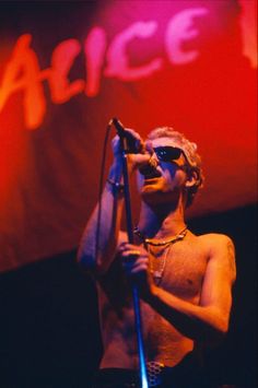 a shirtless man holding a microphone in front of a red and white sign that reads alice